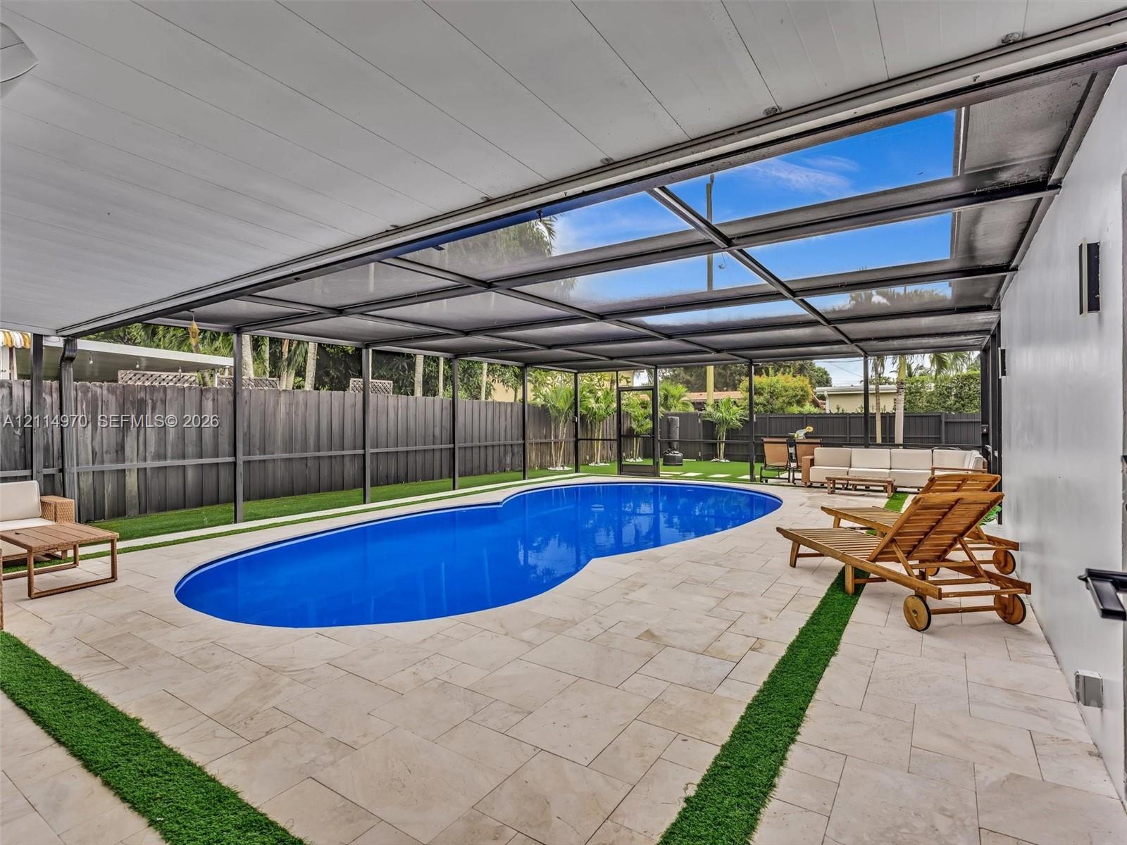 Screen-enclosed patio area featuring an inground pool, stone-paver decking, integrated turf borders, and perimeter privacy fencing