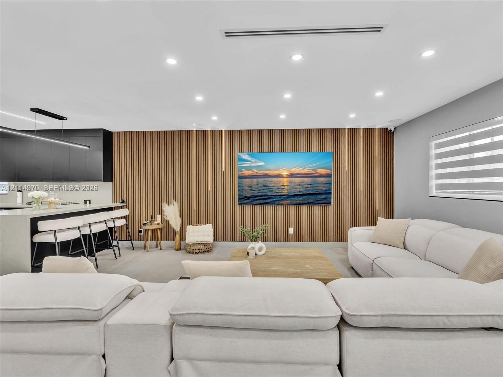 Slatted wood accent wall with integrated linear lighting, recessed ceiling lighting, kitchen island with stone-surface countertop, and matte black cabinetry