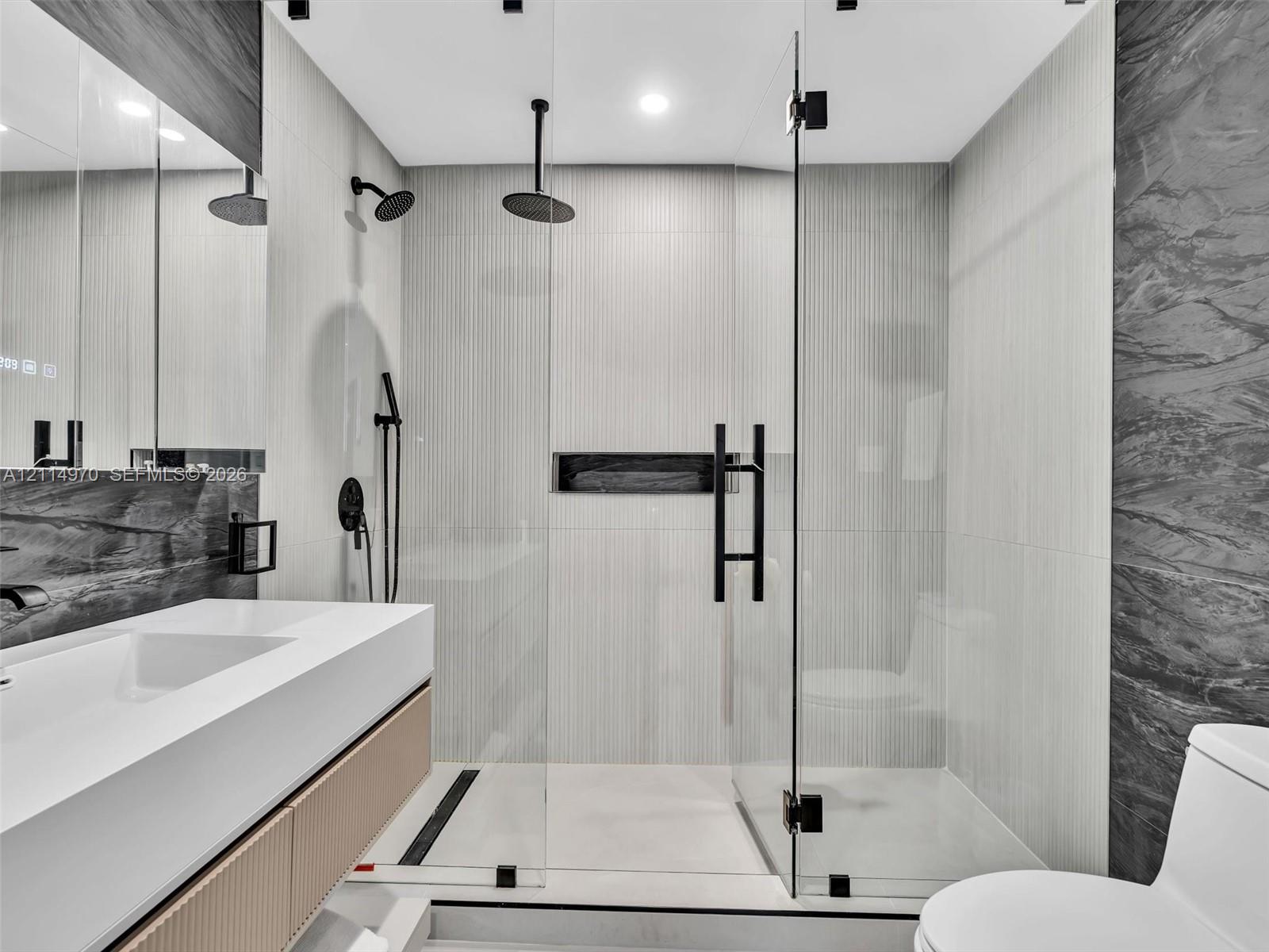 Floating vanity with integrated sink, walk-in shower featuring a frameless glass enclosure, ceiling-mounted rainfall showerhead, matte black hardware, and built-in wall niche