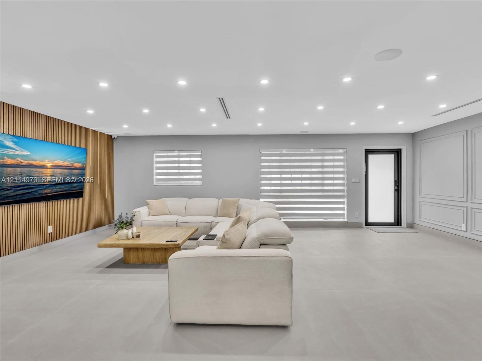 Spacious interior featuring a vertical wood-slat accent wall, neutral large-format tile flooring, recessed ceiling lighting, and decorative wall molding