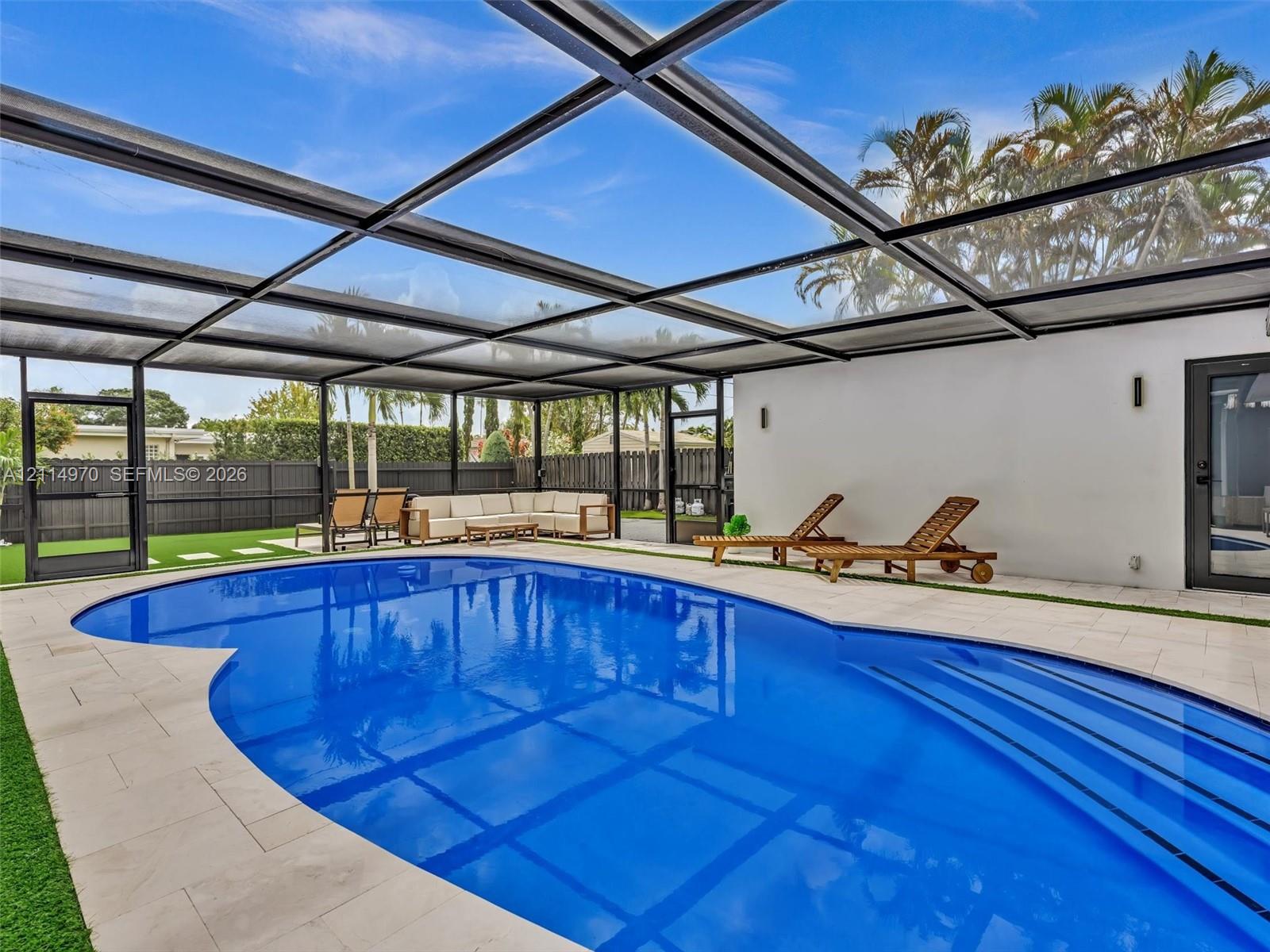 Screened-in patio featuring a swimming pool with integrated stairs, light-toned stone tile decking, and a privacy fence
