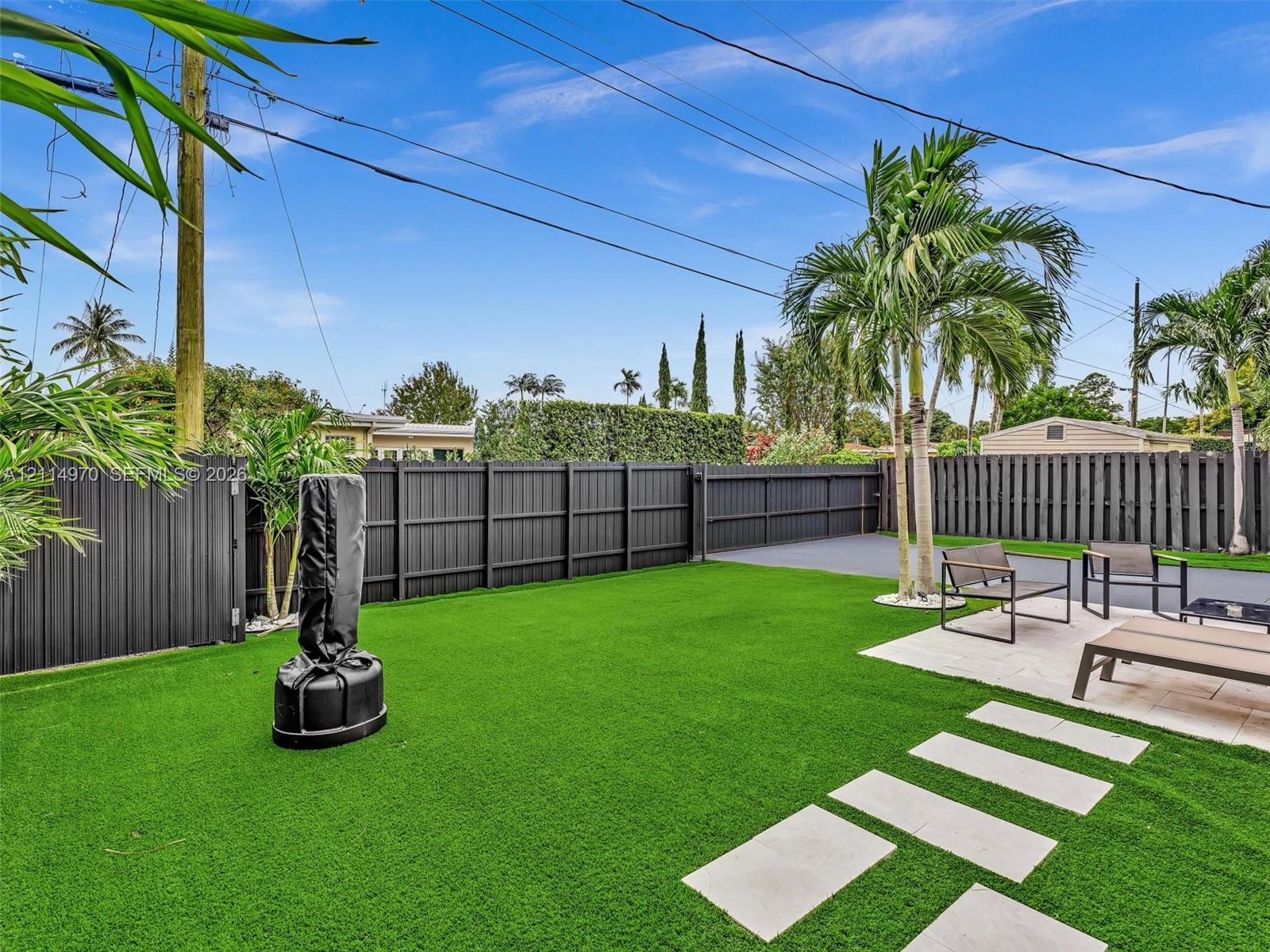 Backyard featuring synthetic turf, paver patio, tall privacy fencing, and established palm trees