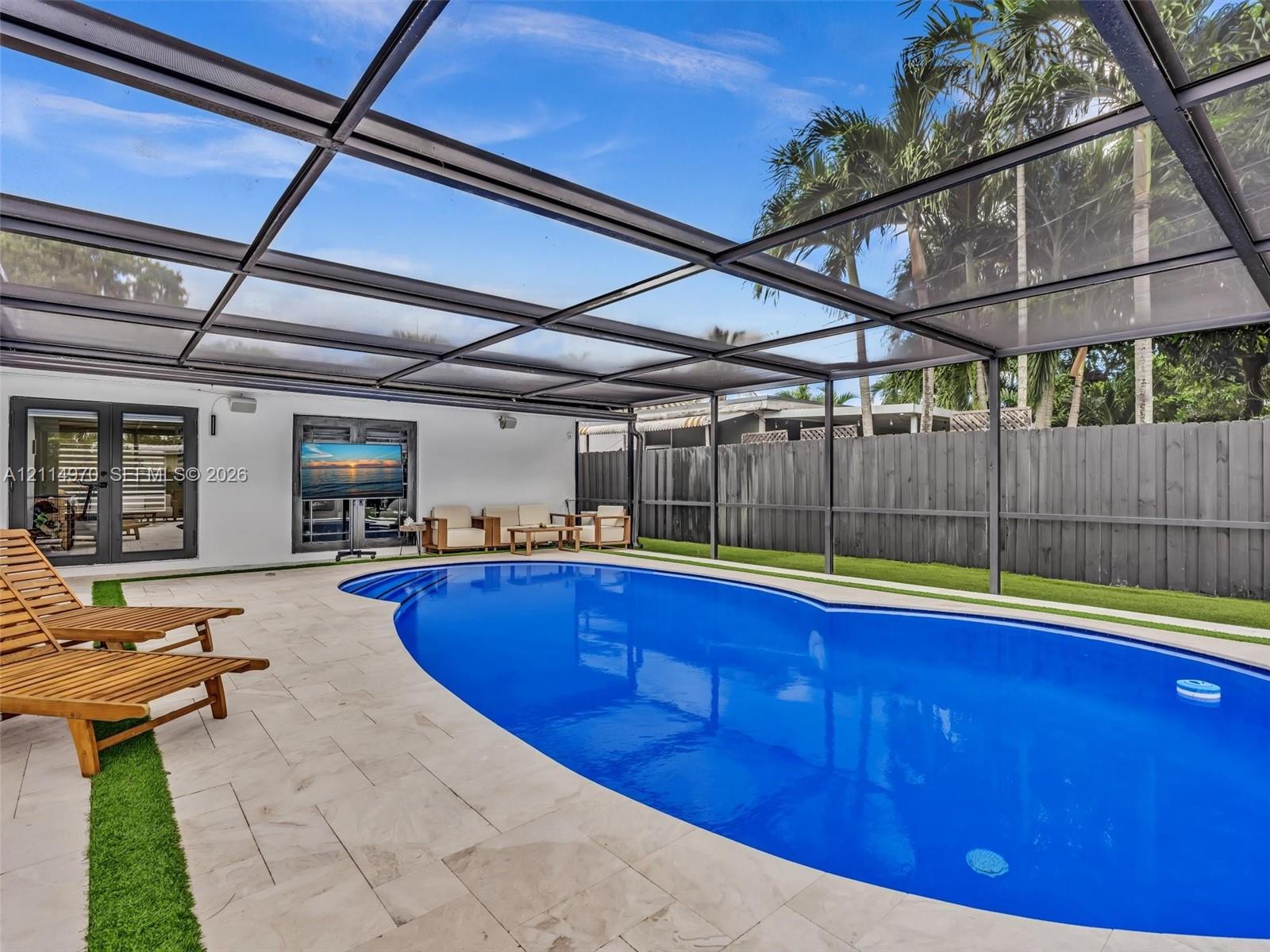 Screened-in pool area featuring light-toned stone decking, inset synthetic turf, a built-in step entry, and dark-finished metal framing