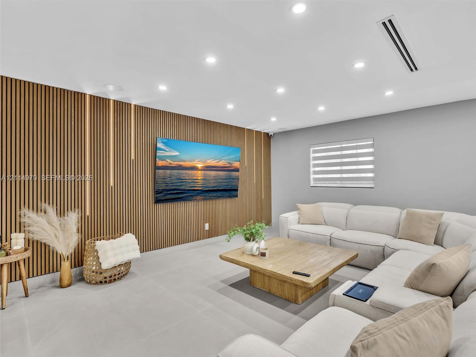 Vertical wood-slat accent wall with integrated LED lighting, neutral large-format tile flooring, recessed ceiling lighting, and dual-roller window shade
