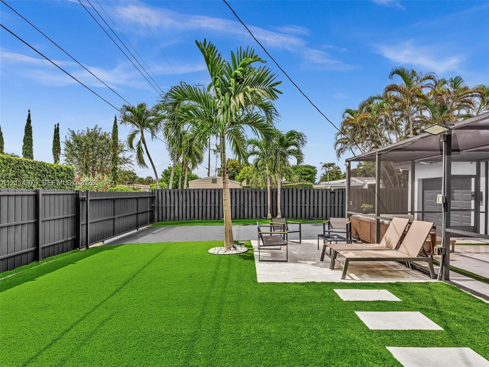 Fenced backyard featuring synthetic turf, stone paver pathway, screened-in patio, and mature palm trees