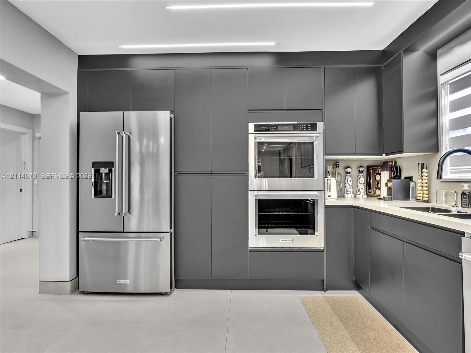 Contemporary kitchen featuring matte charcoal cabinetry, stainless steel double wall ovens, a matching French-door refrigerator, integrated linear ceiling lighting, and solid-surface countertops Contemporary kitchen featuring matte charcoal cabinetry, stainless steel double wall ovens, a matching French-door refrigerator, integrated linear ceiling lighting, and solid-surface countertops