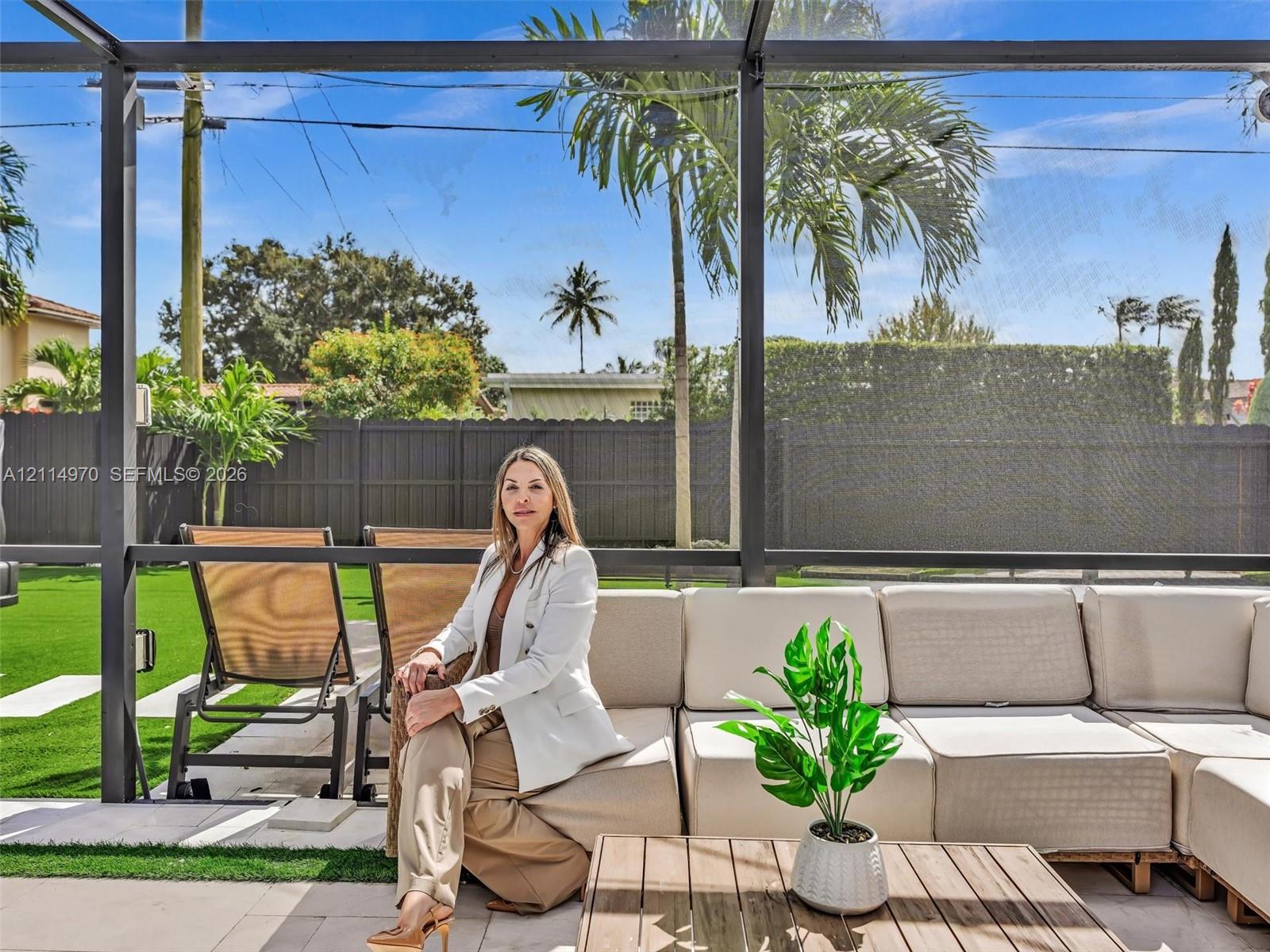 Screened-in outdoor living area featuring paved patio flooring, synthetic turf lawn, and solid perimeter fencing