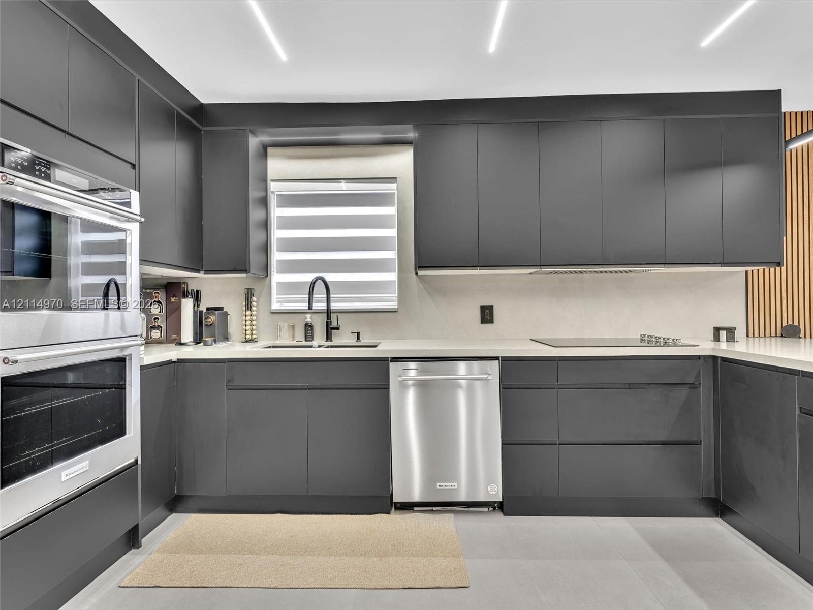 Contemporary kitchen featuring matte charcoal cabinetry, stainless steel double wall ovens and dishwasher, solid-surface countertops, and recessed linear ceiling lighting Contemporary kitchen featuring matte charcoal cabinetry, stainless steel double wall ovens and dishwasher, solid-surface countertops, and recessed linear ceiling lighting