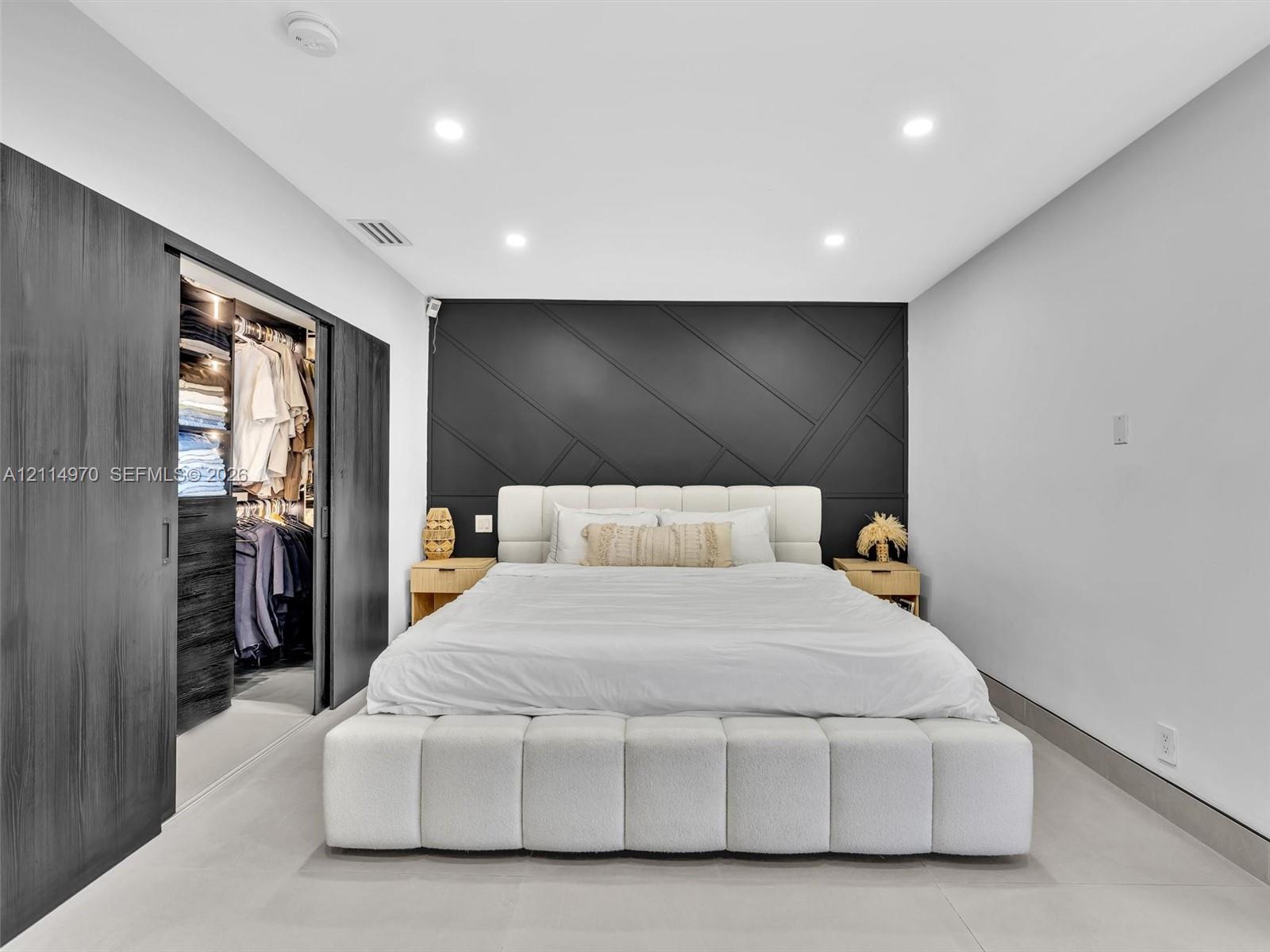 Accent wall with geometric trim detail, sliding dark-finish wardrobe doors, integrated recessed lighting, and large-format tile flooring