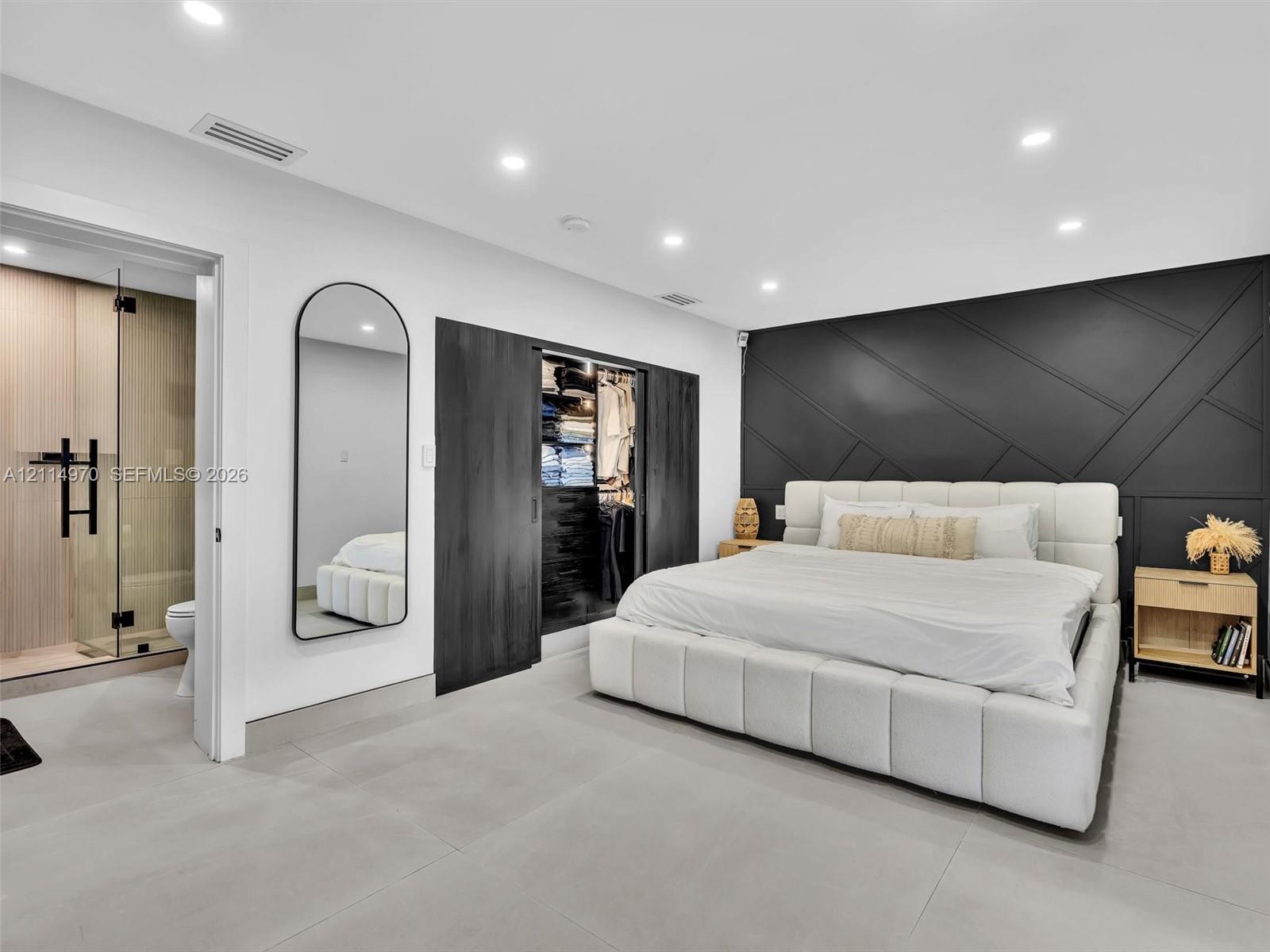 Geometric-patterned accent wall, sliding-door walk-in closet, recessed ceiling lighting, and large-format tile flooring Geometric-patterned accent wall, sliding-door walk-in closet, recessed ceiling lighting, and large-format tile flooring