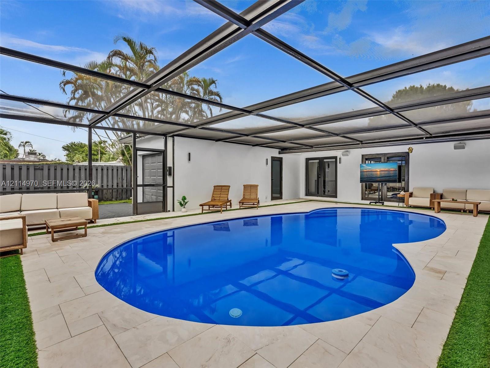 Screen-enclosed patio featuring a swimming pool, stone paver decking, synthetic turf accents, and wall-mounted exterior lighting