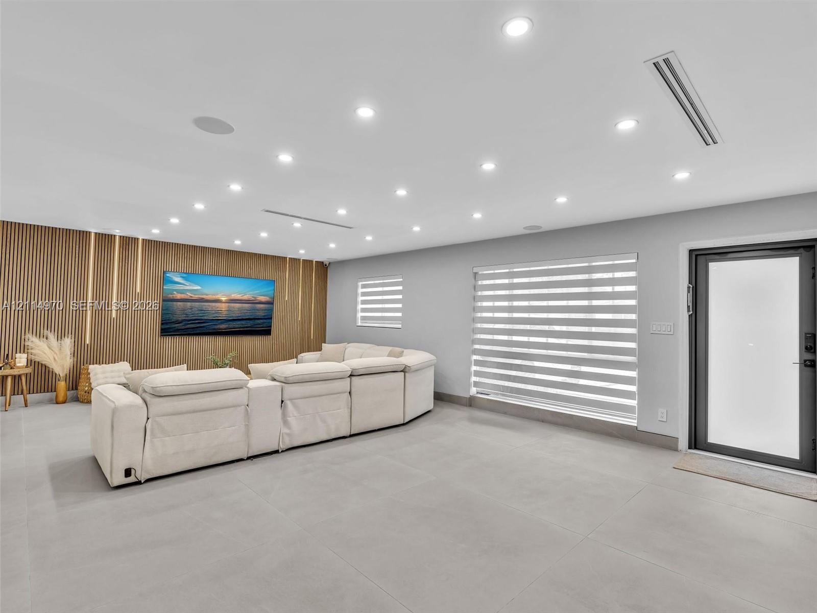 Vertical wood-slat accent wall, neutral large-format tile flooring, recessed ceiling lighting, horizontal banded window shades, and exterior-grade door with frosted glass panel