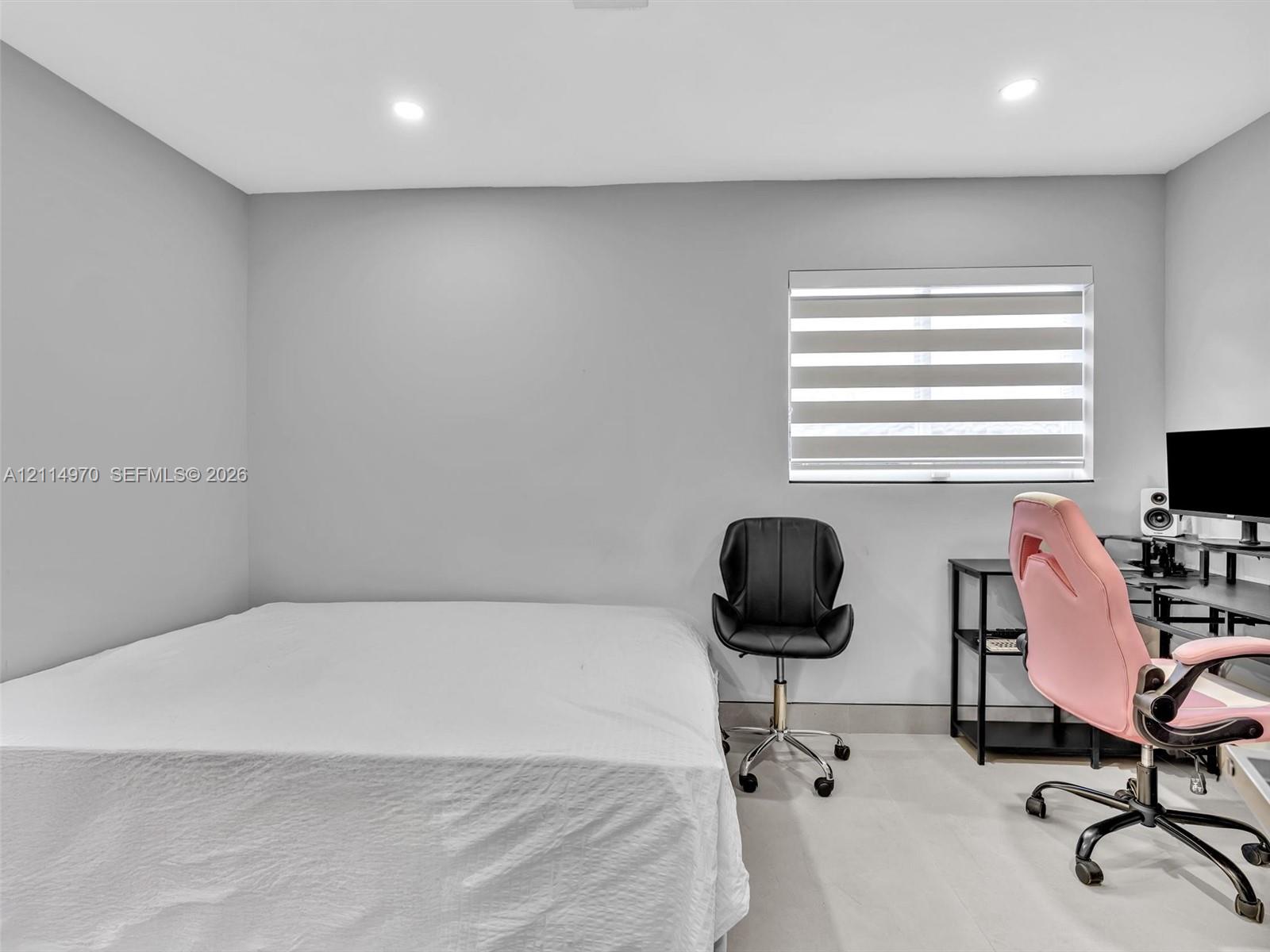 Neutral interior space featuring smooth walls, recessed ceiling lighting, light-toned flooring, and a window equipped with banded roller shades