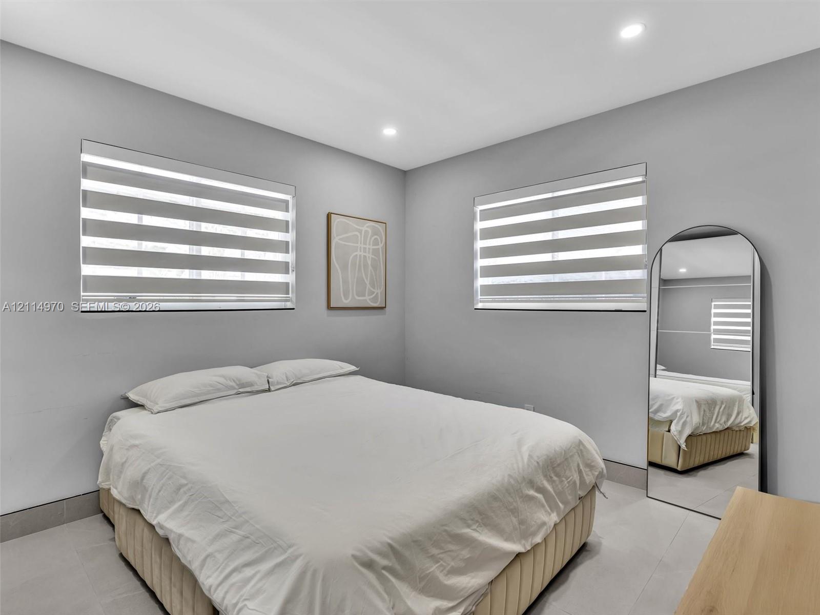 Neutral-toned interior space featuring light-colored tile flooring, recessed ceiling lighting, and dual windows equipped with horizontal light-filtering roller shades