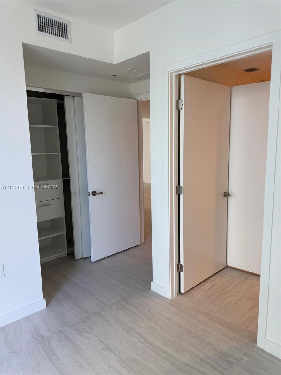Interior space featuring wood-finish flooring, white solid-core doors with brushed nickel hardware, and built-in closet storage with integrated shelving and drawers