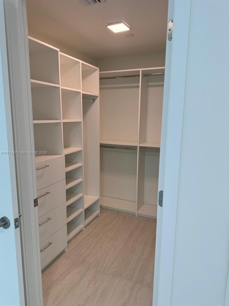 Walk-in closet featuring white built-in shelving, integrated dresser drawers with metal hardware, double-tier hanging rods, and wood-finish flooring