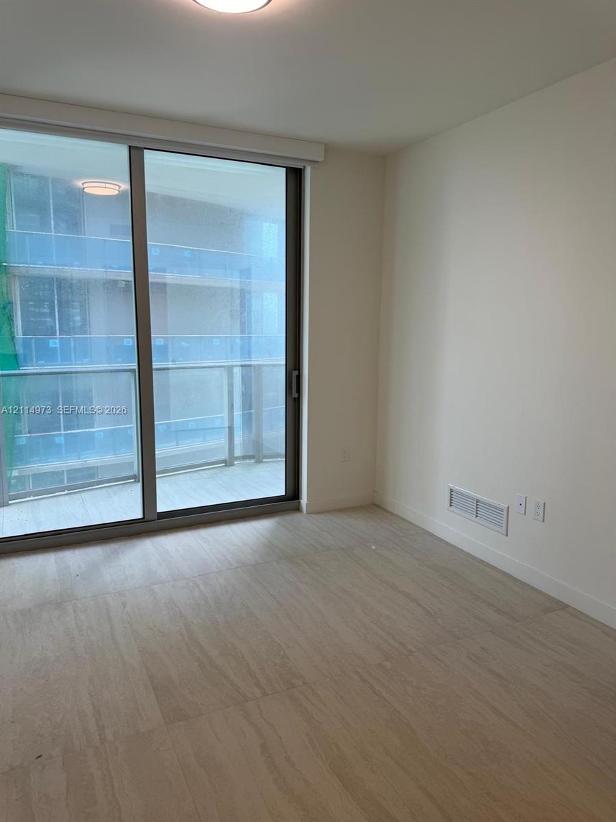 Floor-to-ceiling sliding glass door, private balcony with glass railing, and wood-finish flooring