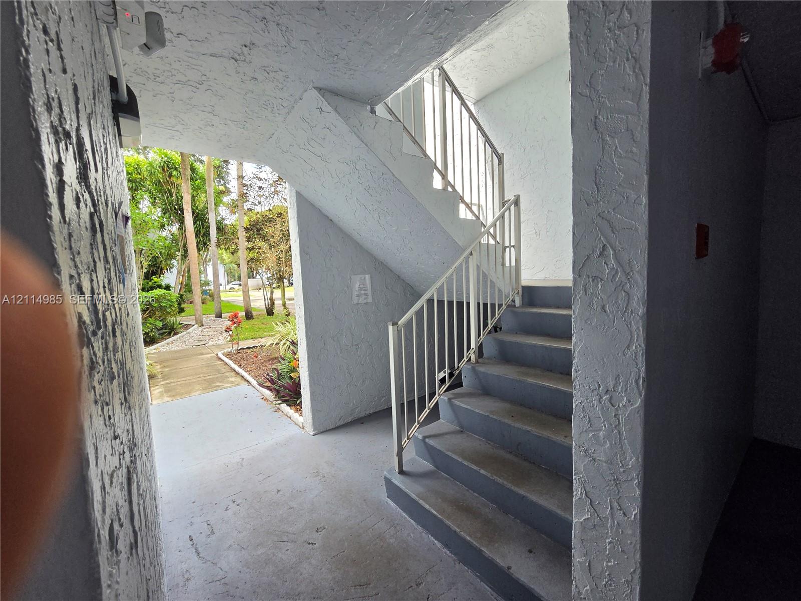 Exterior staircase with metal railings, concrete steps, and textured stucco walls