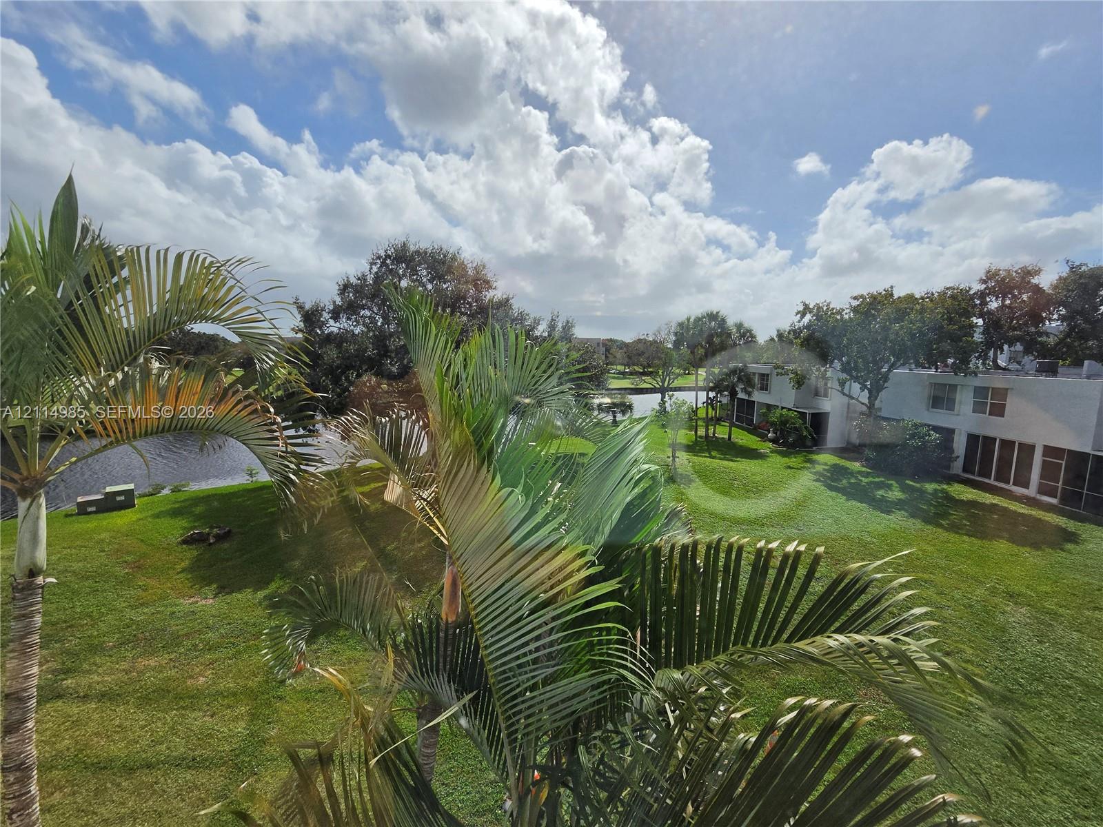 Expansive green space featuring mature palm trees, a pond, and residential structures with exterior white siding