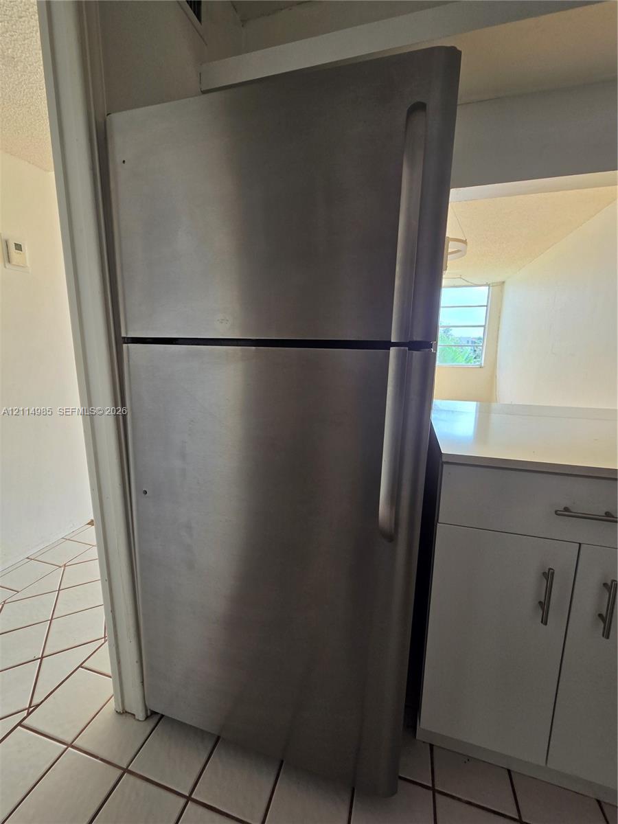 Stainless steel top-freezer refrigerator, white cabinetry with silver-tone hardware, and white ceramic floor tile