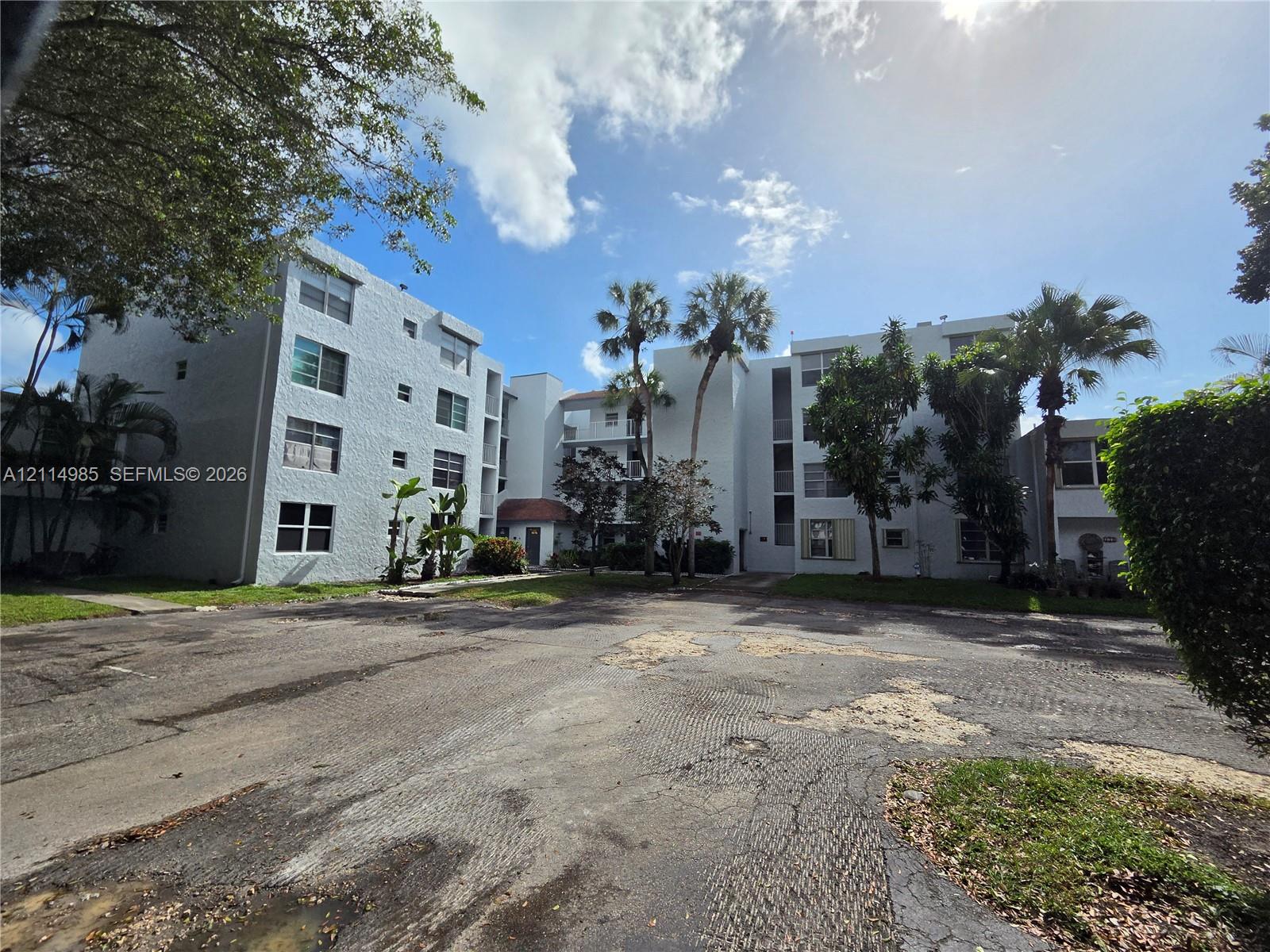 Multi-story stucco exterior featuring multiple rectangular windows, palm trees, and mature landscaping