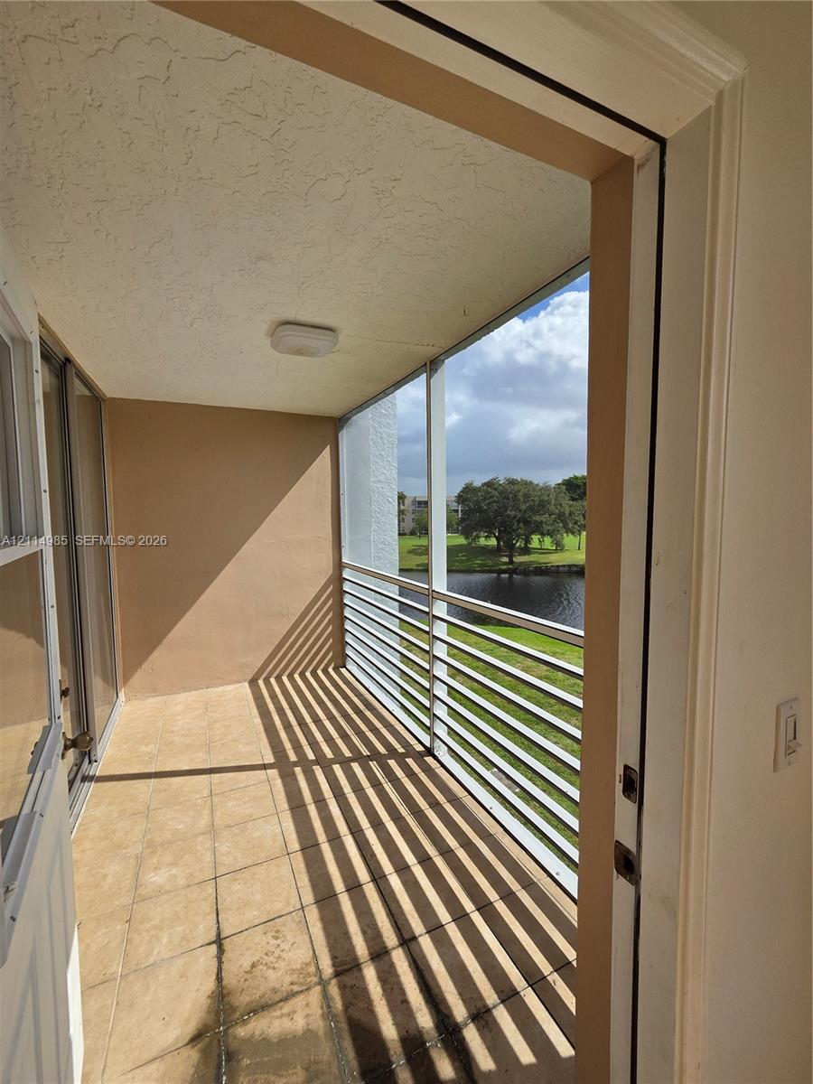Covered balcony featuring tile flooring, a screened enclosure, and aluminum railings with water scenery
