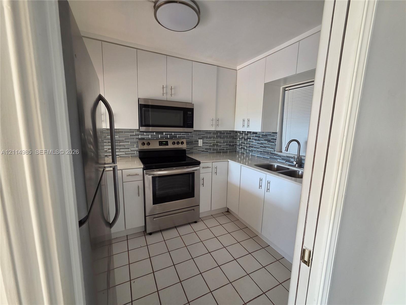 Kitchen featuring stainless steel appliances, white cabinetry, light-toned countertops, multi-toned tile backsplash, and square floor tiling
