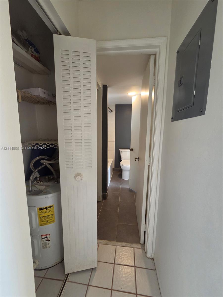 Utility closet featuring louvered bi-fold doors, white ceramic tile flooring, and integrated water heater