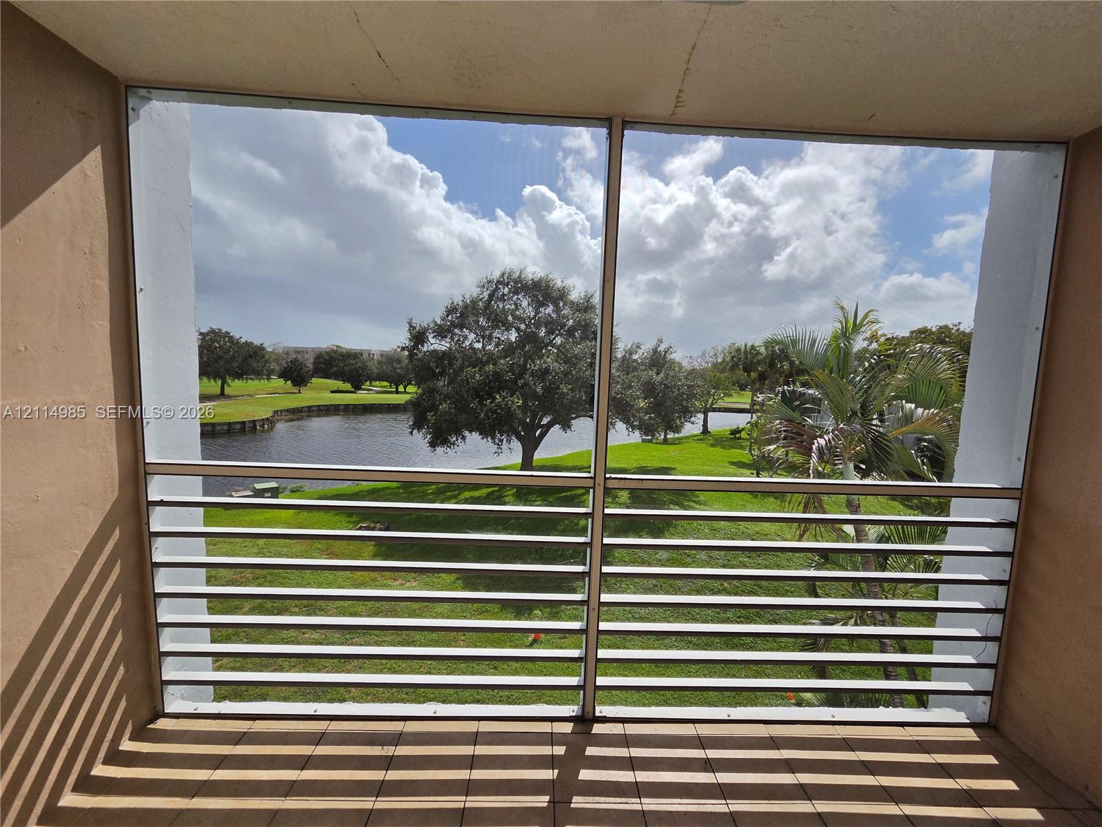 Screened-in balcony featuring tile flooring and horizontal metal railings overlooking a water feature and manicured grounds