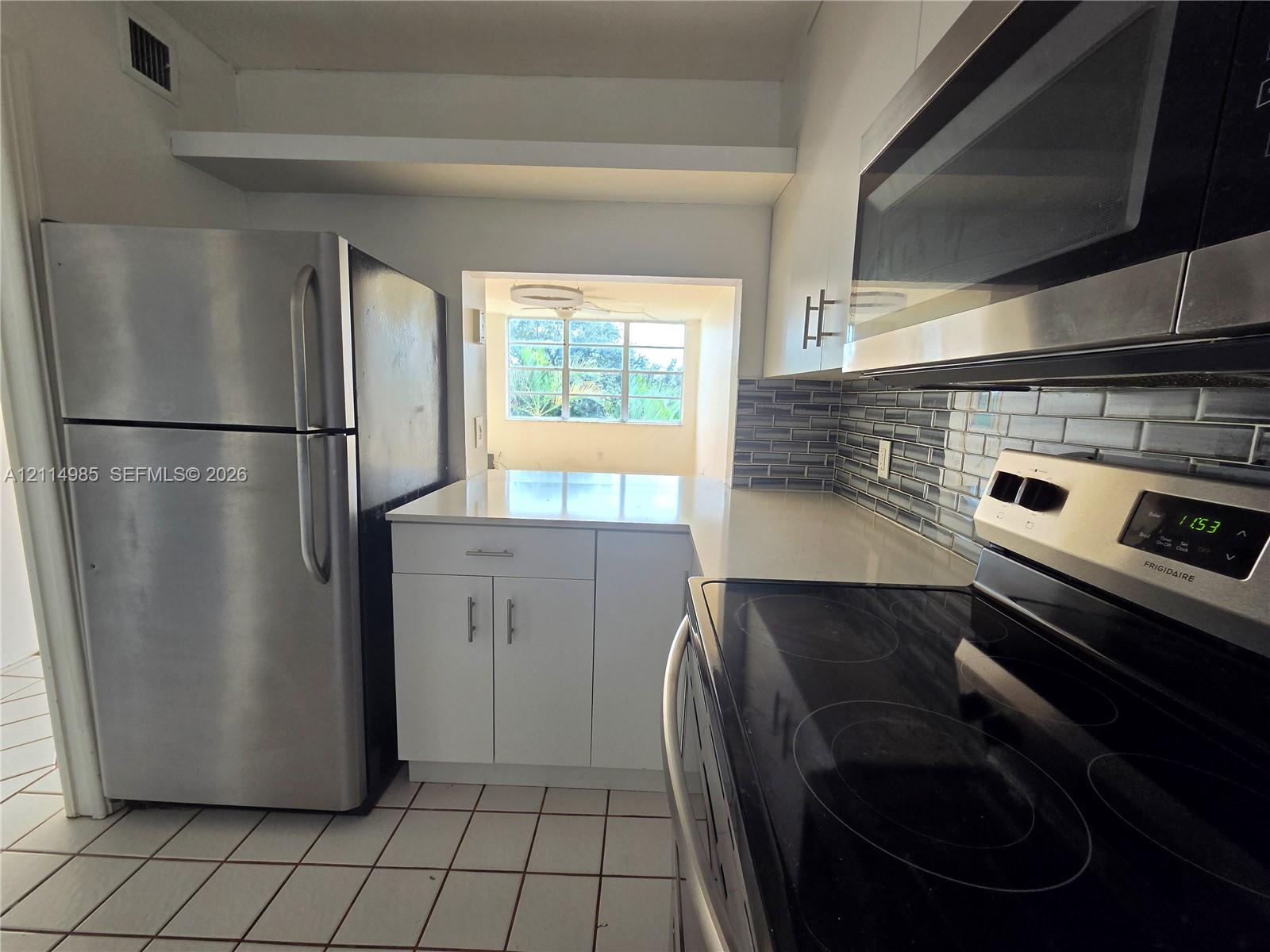 Kitchen featuring white cabinetry, solid-surface countertops, stainless steel appliances, and a tiled backsplash