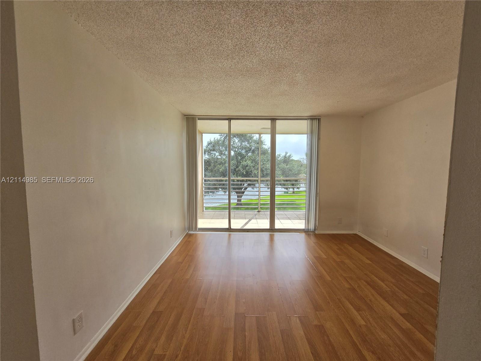 Interior space featuring wood-finish flooring, textured ceiling, and floor-to-ceiling sliding glass doors opening to an exterior balcony