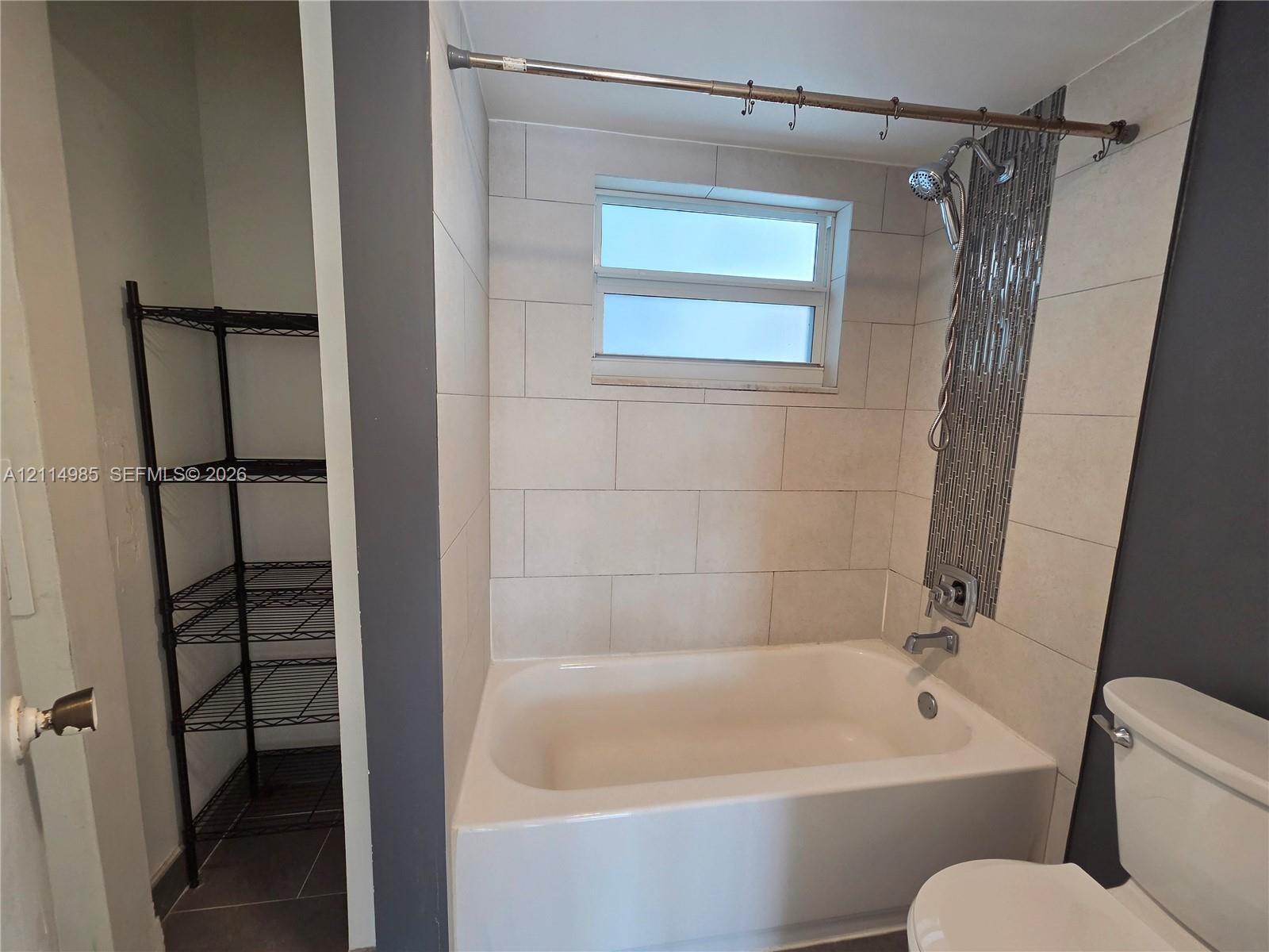 Bathtub with large-format ceramic tile surround, vertical decorative mosaic tile accent, and built-in storage alcove