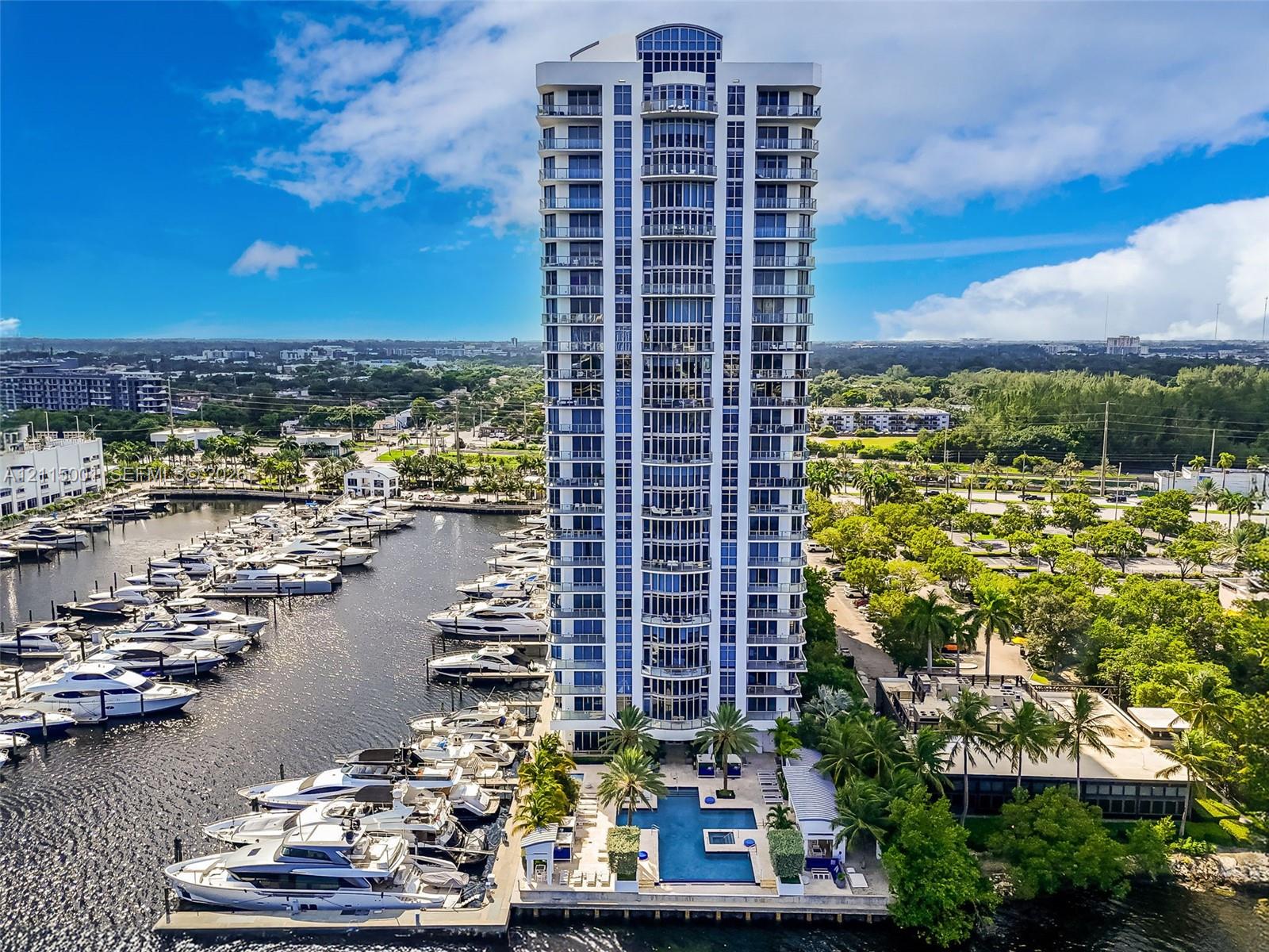 High-rise tower featuring extensive glass balcony railings, a ground-level swimming pool, and direct access to a private deep-water marina