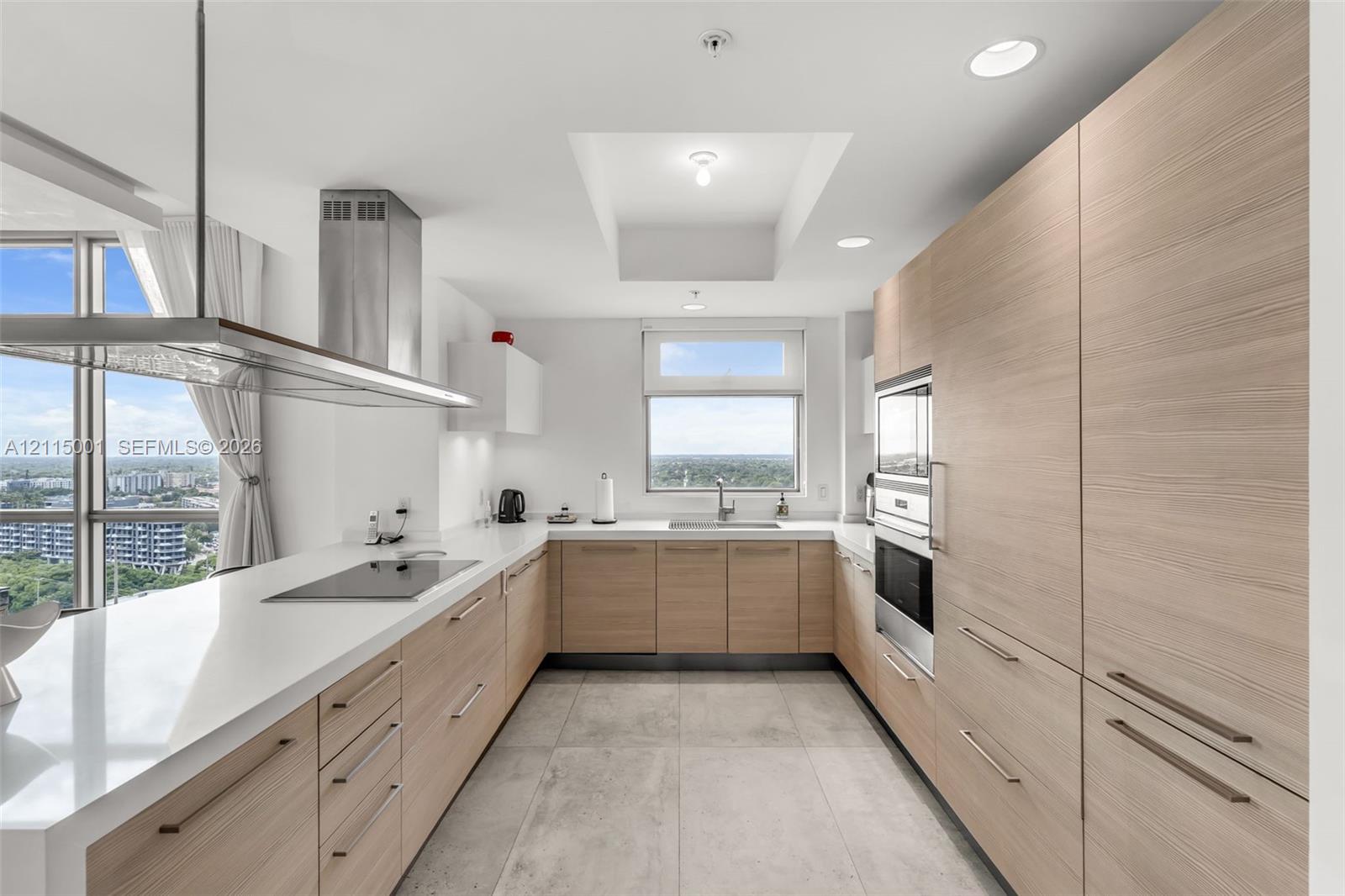 Kitchen featuring light-tone wood-finish cabinetry, white countertops, recessed lighting, a stainless steel range hood, and large-format tile flooring