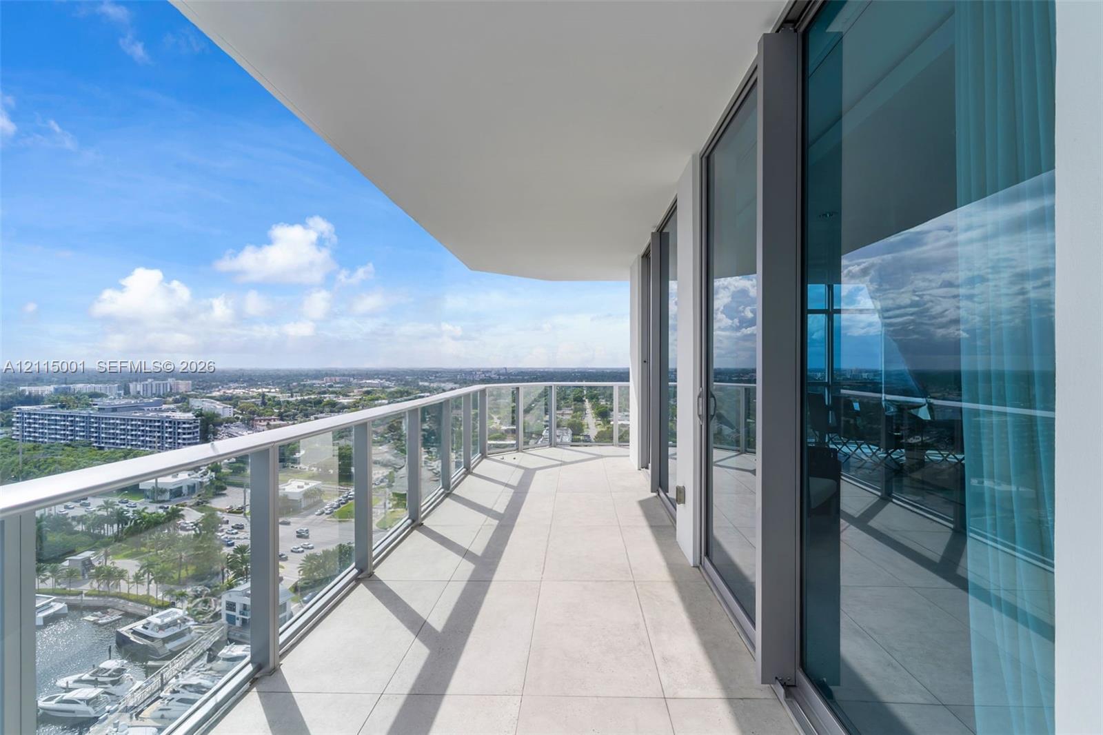 Covered balcony featuring oversized tile flooring, full-height glass sliding doors, and a transparent glass railing