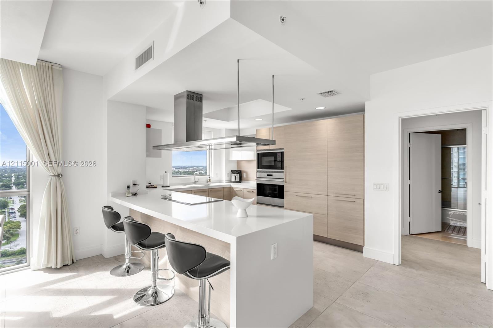 Kitchen featuring quartz countertops, flat-panel wood-finish cabinetry, stainless steel built-in oven and microwave, and a stainless steel suspended range hood