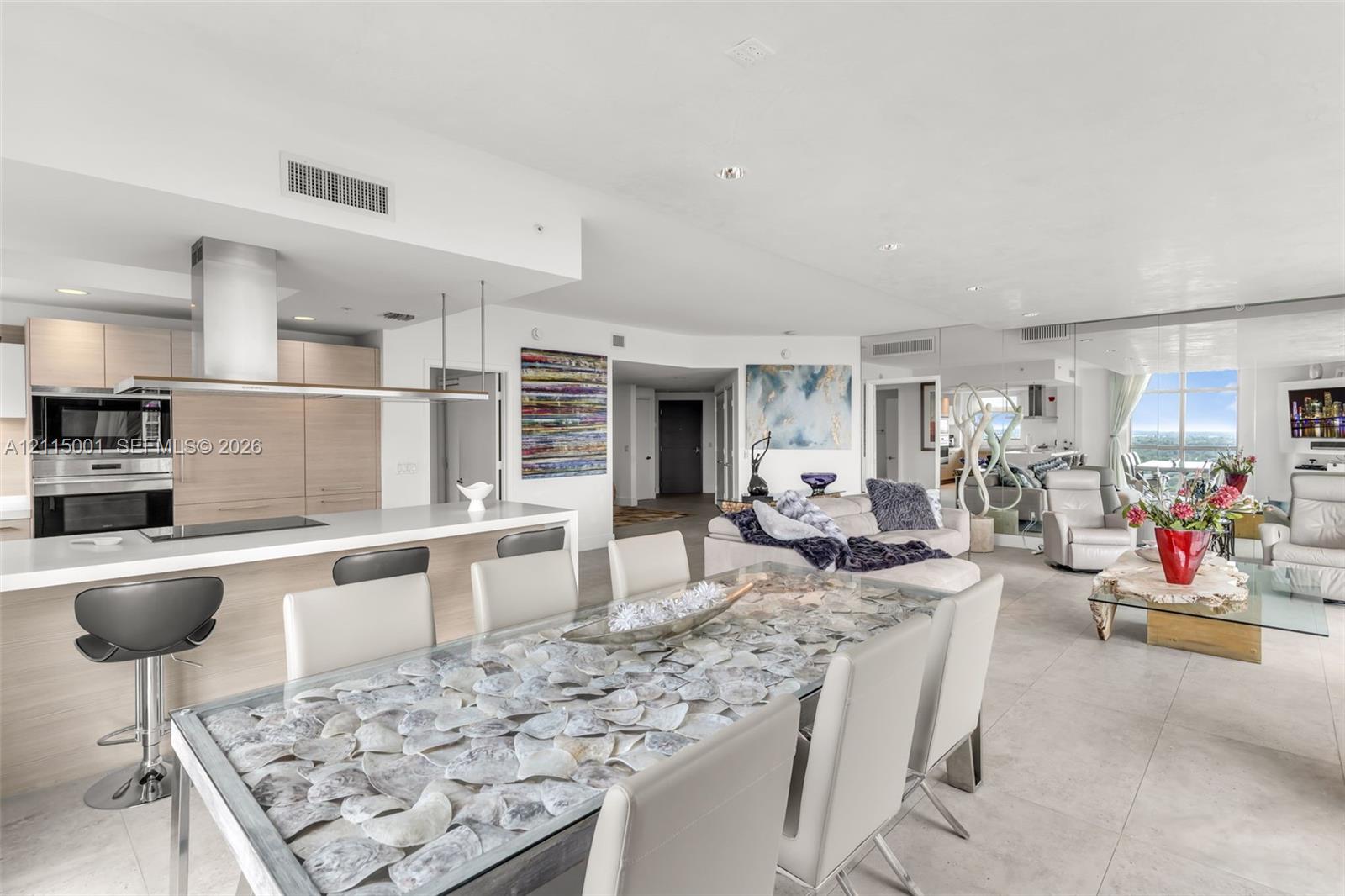 Open-concept kitchen featuring light wood-finish cabinetry, a white countertop island, and stainless steel wall-mounted oven and microwave Open-concept kitchen featuring light wood-finish cabinetry, a white countertop island, and stainless steel wall-mounted oven and microwave