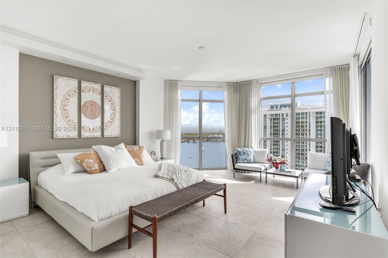 Floor-to-ceiling windows, neutral tile flooring, accent wall, and expansive water backdrop Floor-to-ceiling windows, neutral tile flooring, accent wall, and expansive water backdrop
