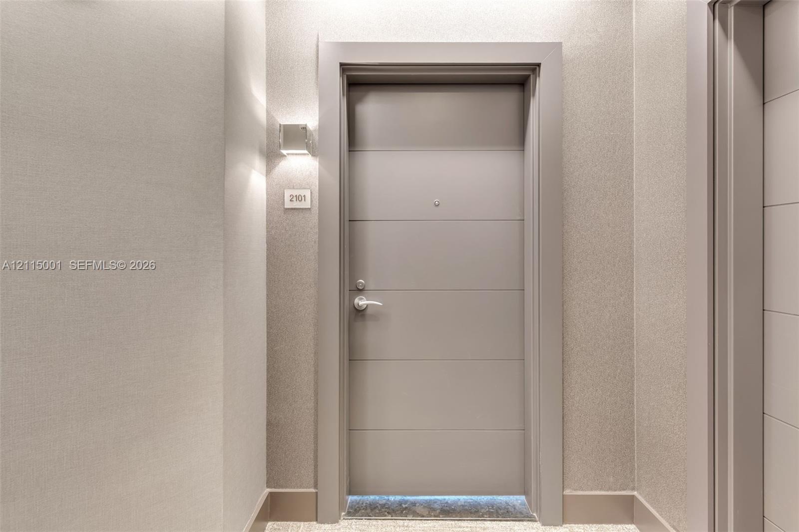 Solid-core entry door featuring horizontal panel detailing, metallic-finish hardware, peephole, and integrated wall-mounted sconce lighting