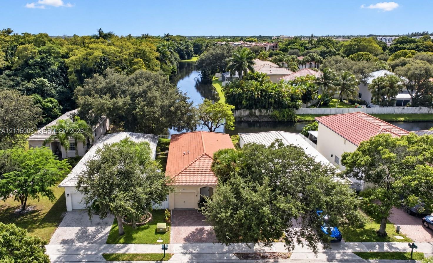 Aerial perspective featuring residences with terracotta-style roof tiles, paved driveways, and mature landscaping situated along a waterway