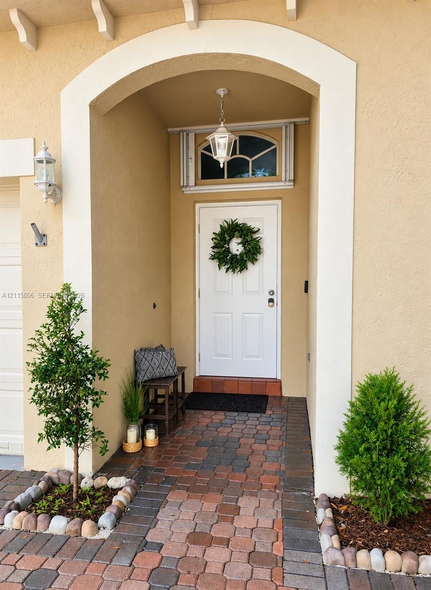 Covered entryway featuring a recessed arched opening, decorative transom window, pendant lantern fixture, and multi-tonal paver hardscaping Covered entryway featuring a recessed arched opening, decorative transom window, pendant lantern fixture, and multi-tonal paver hardscaping