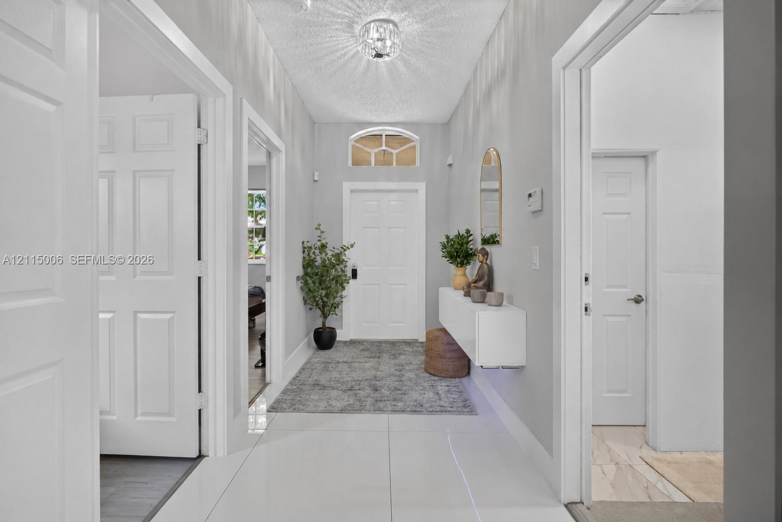 Entryway featuring large-format tile flooring, a six-panel entry door with an arched transom window, a wall-mounted floating console, and a central crystal-style flush-mount light fixture Entryway featuring large-format tile flooring, a six-panel entry door with an arched transom window, a wall-mounted floating console, and a central crystal-style flush-mount light fixture