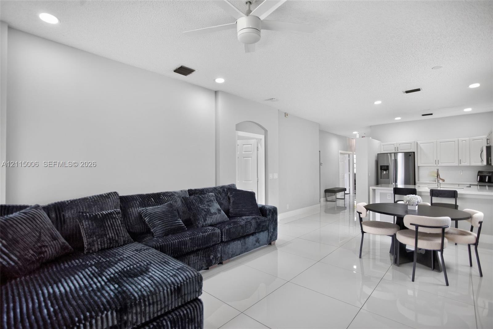 Large-format tile flooring, recessed ceiling lighting, ceiling fan, and white kitchen cabinetry with stainless steel appliances