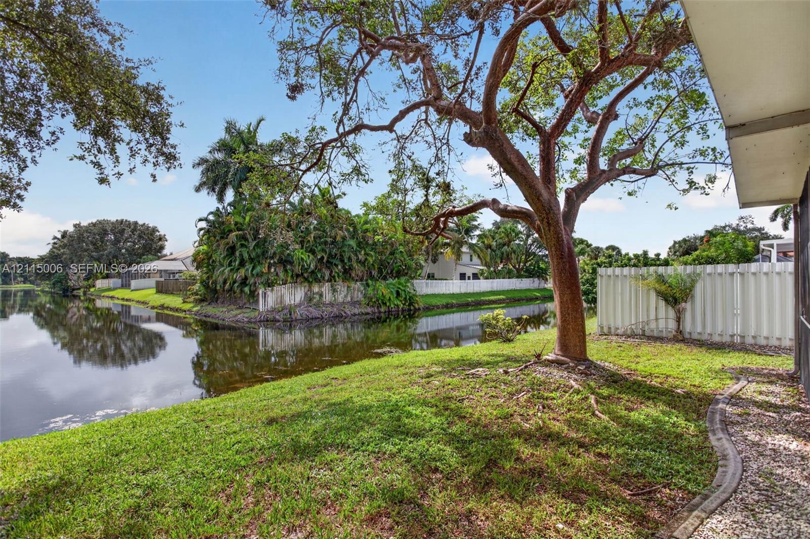 Waterfront lot featuring mature trees, a grass lawn, and a vinyl privacy fence