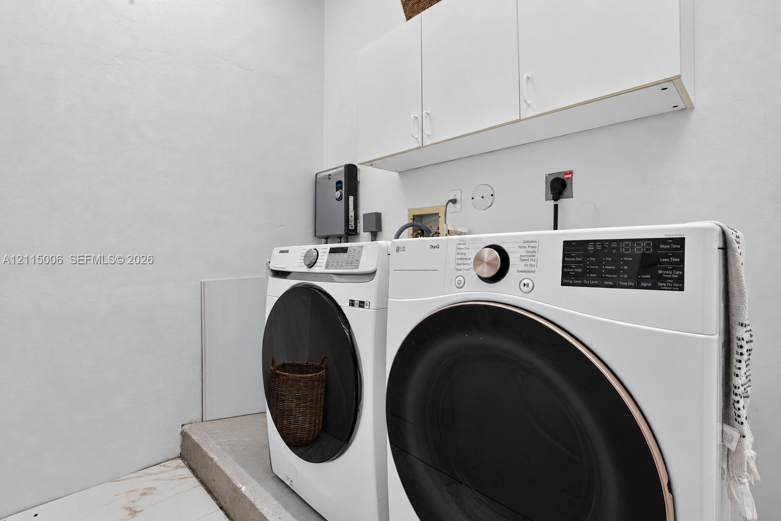 Laundry area featuring white wall-mounted cabinetry and large-format tile flooring