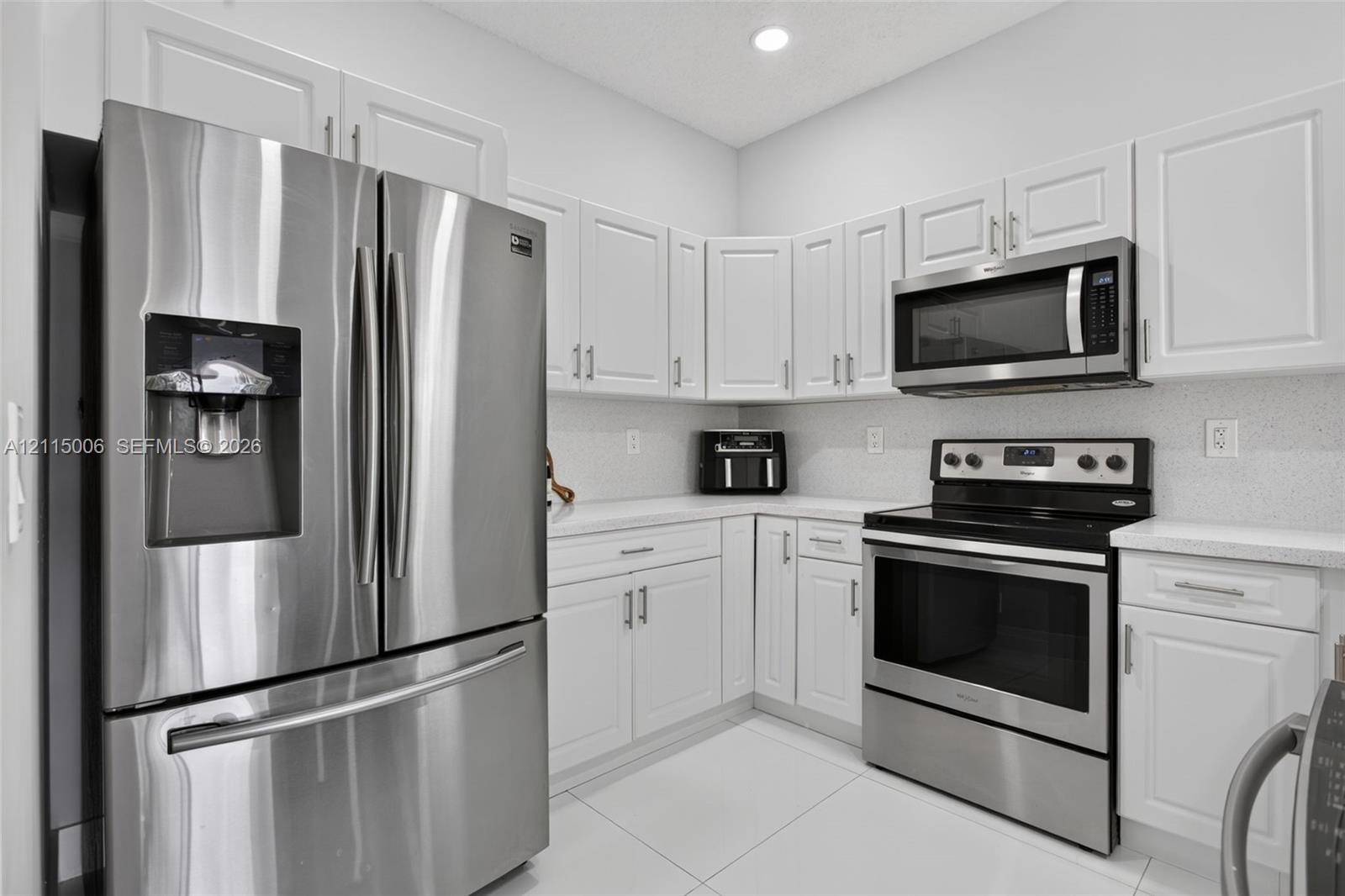 Kitchen featuring white shaker-style cabinetry, stainless steel refrigerator, over-the-range microwave, electric range, and light-toned solid surface countertops