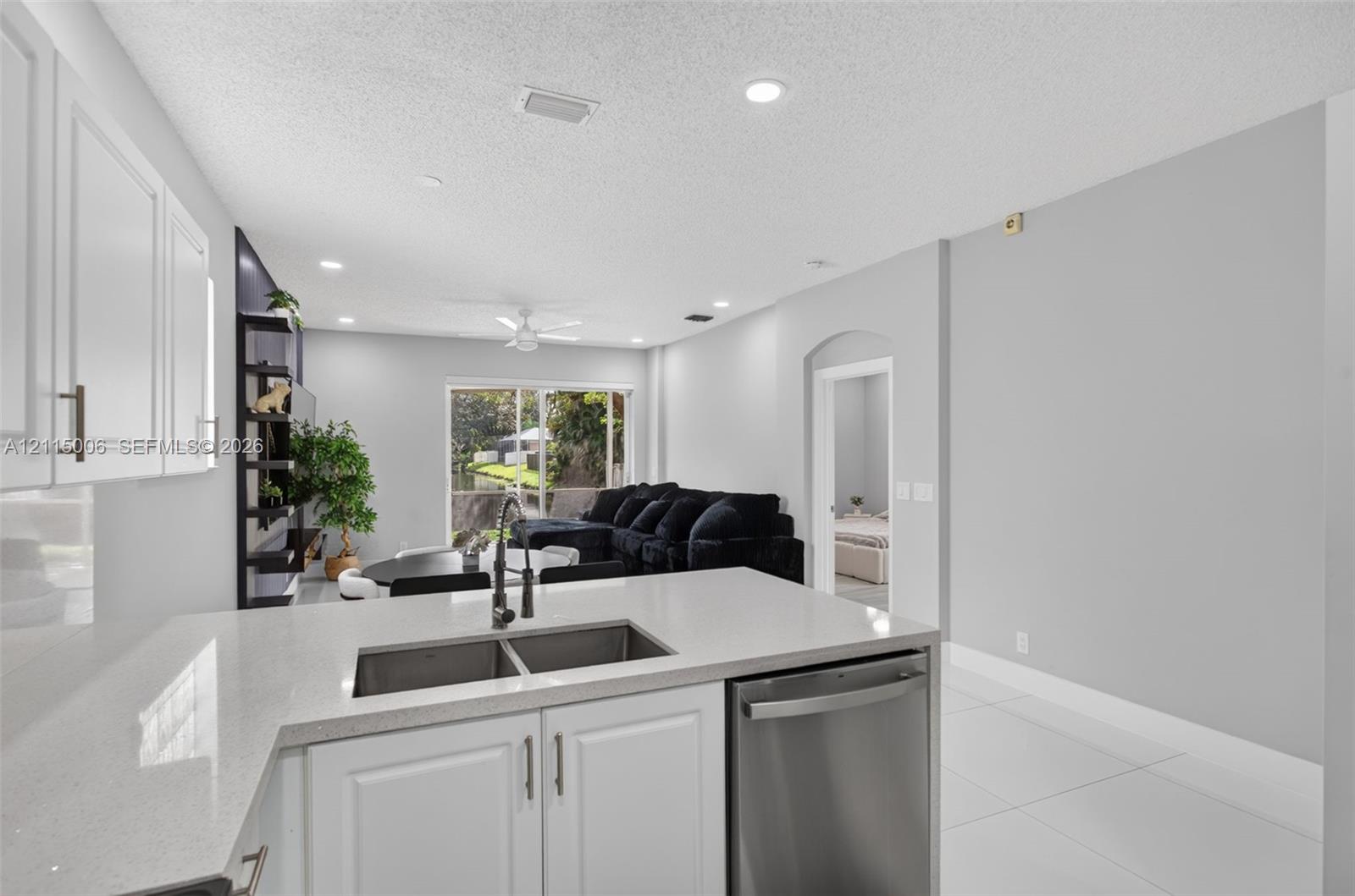 Kitchen featuring white cabinetry, solid-surface countertops, dual-basin stainless steel sink, and stainless steel dishwasher, complemented by tile flooring throughout