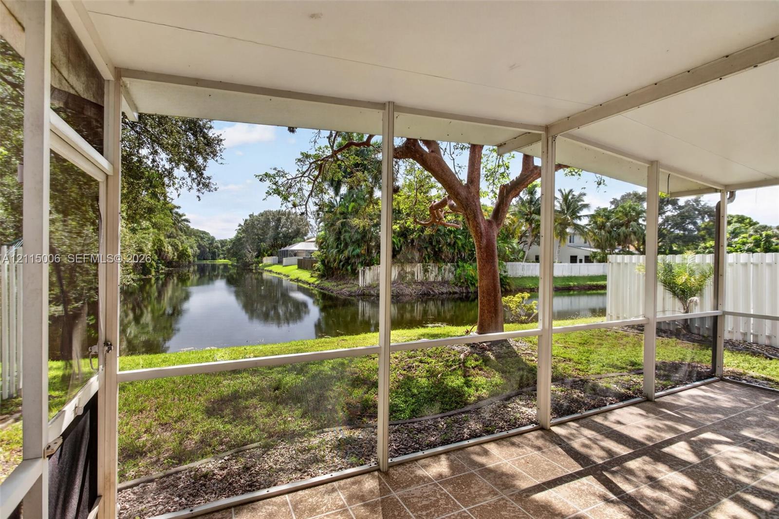 Screened-in lanai featuring tile flooring, a solid ceiling, and water frontage with mature trees