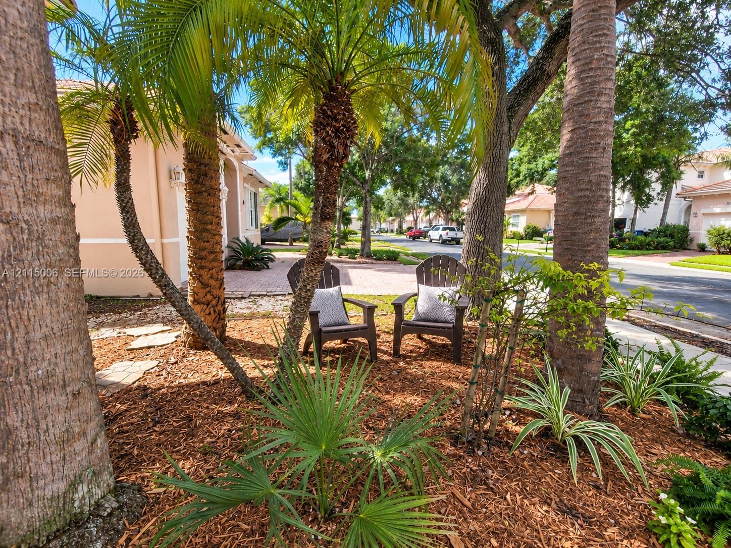 Landscaped front grounds featuring mature palm trees, diverse ornamental shrubbery, stone-paver hardscaping, and mulch bedding