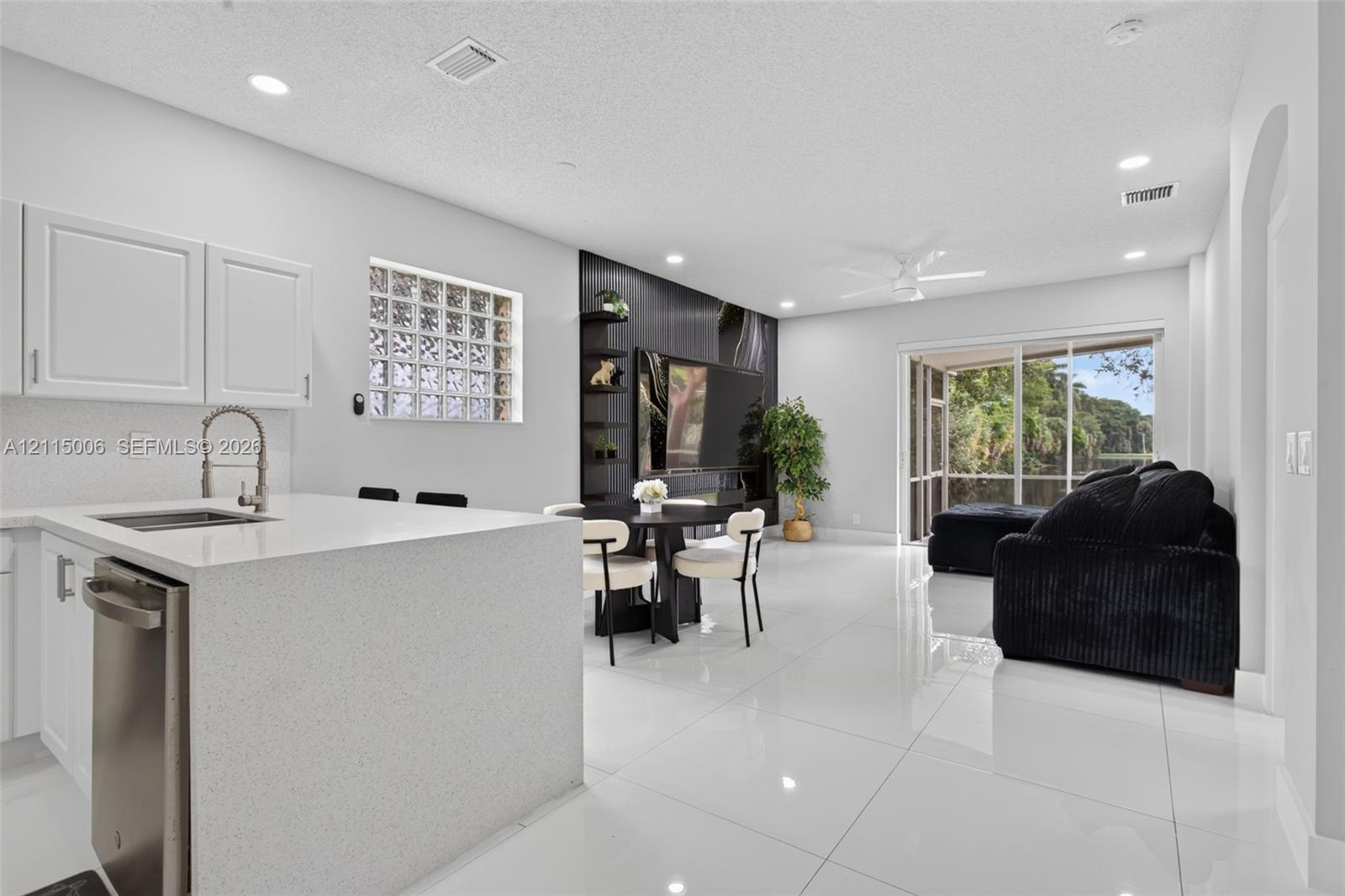 Kitchen featuring a waterfall-edge quartz island, stainless steel dishwasher, glass block accent window, and high-gloss floor tile